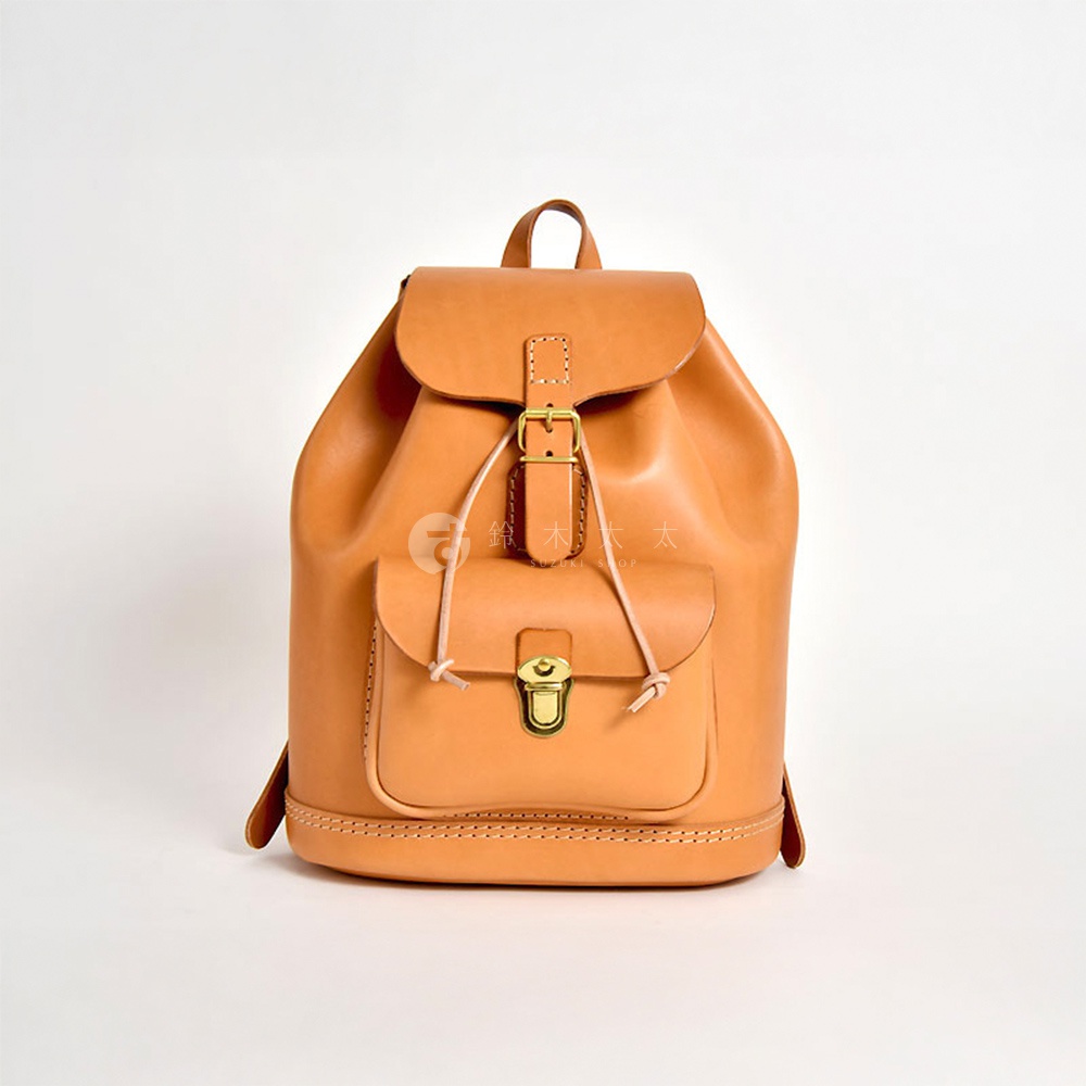鞣製皮革製作的經典後背包，呈現自然棕色皮革質感，設有束繩閉合、翻蓋和金色鎖扣前袋，適合日常攜帶。