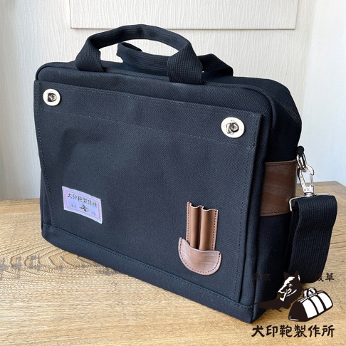 黑色純綿帆布製成，橫式側背包，配有兩個手提把，一個可拆卸式肩帶，銀色金屬扣件，以及棕色皮革裝飾細節。