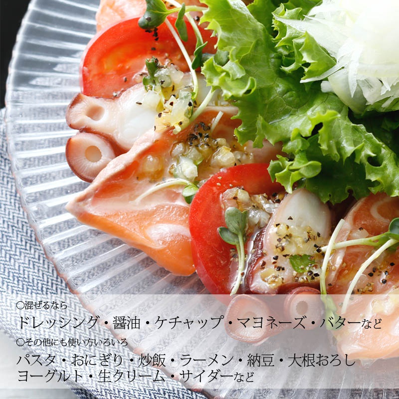 盤狀玻璃盤中盛有鮭魚片、章魚腳、番茄切片、生菜和豆芽菜，淋上醬汁，部分食材帶有香草和黑胡椒粒。