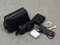 黑色皮革拉鍊收納包，搭配金色拉鍊，旁邊放置黑色數位相機、黑色行動電源、白色無線耳機充電盒、白色耳機及充電線。