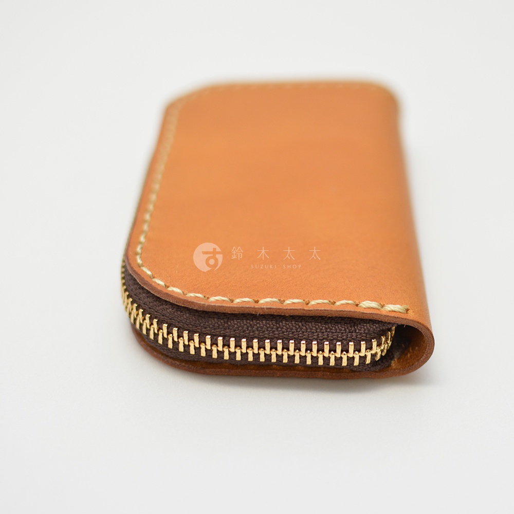 職人手作的淺棕色皮革橢圓形拉鍊鑰匙包，細緻的縫線與金屬拉鍊，質感優良。