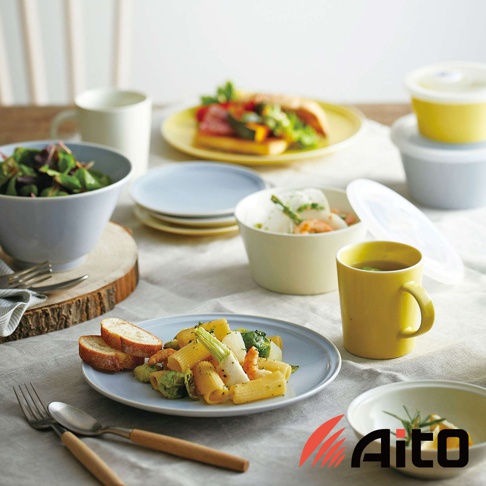 淺藍色主菜盤盛有義大利麵、蔬菜和蝦仁，旁邊放著兩片麵包，以及一套木柄餐具。背景有淺藍色、黃色和米色碗盤、杯子和儲物罐，以及一盤沙拉。