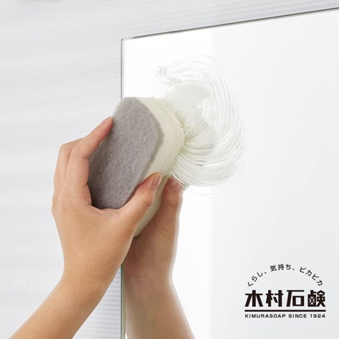 手持灰色海綿刷，正在清潔鏡面，刷毛上帶有白色清潔泡沫，鏡面反射出使用者的手部。
