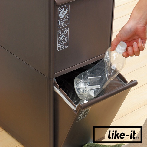 棕色塑膠三層分類垃圾桶，其中一層可抽出，正有人將塑膠瓶放入。垃圾桶側面有「CAN」、「BIN」等回收標誌。