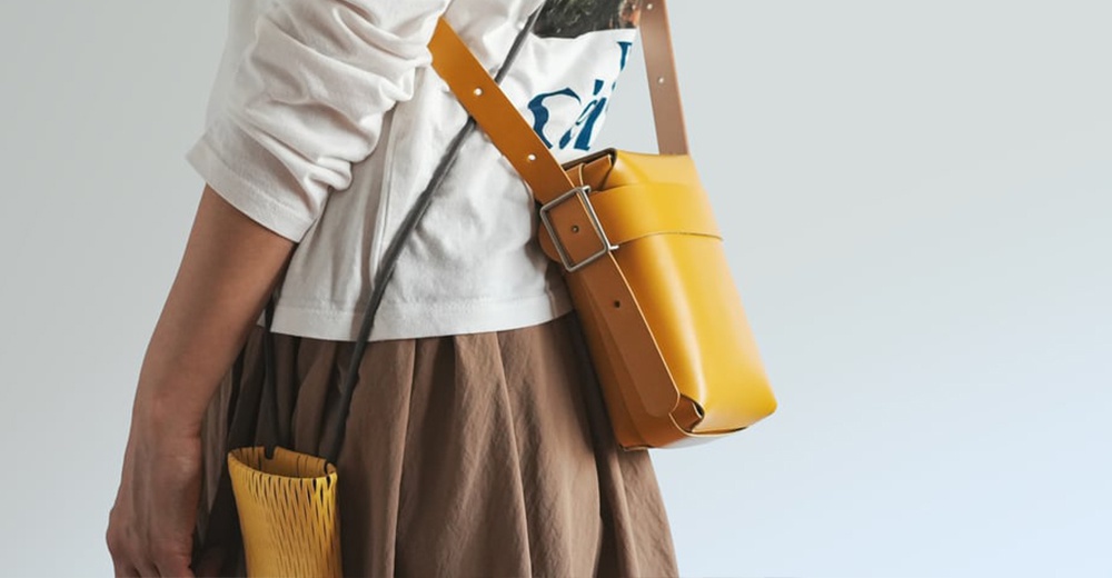 一名身穿白色長袖上衣和棕色長裙的女子，斜揹一個黃色皮革迷你斜背包。