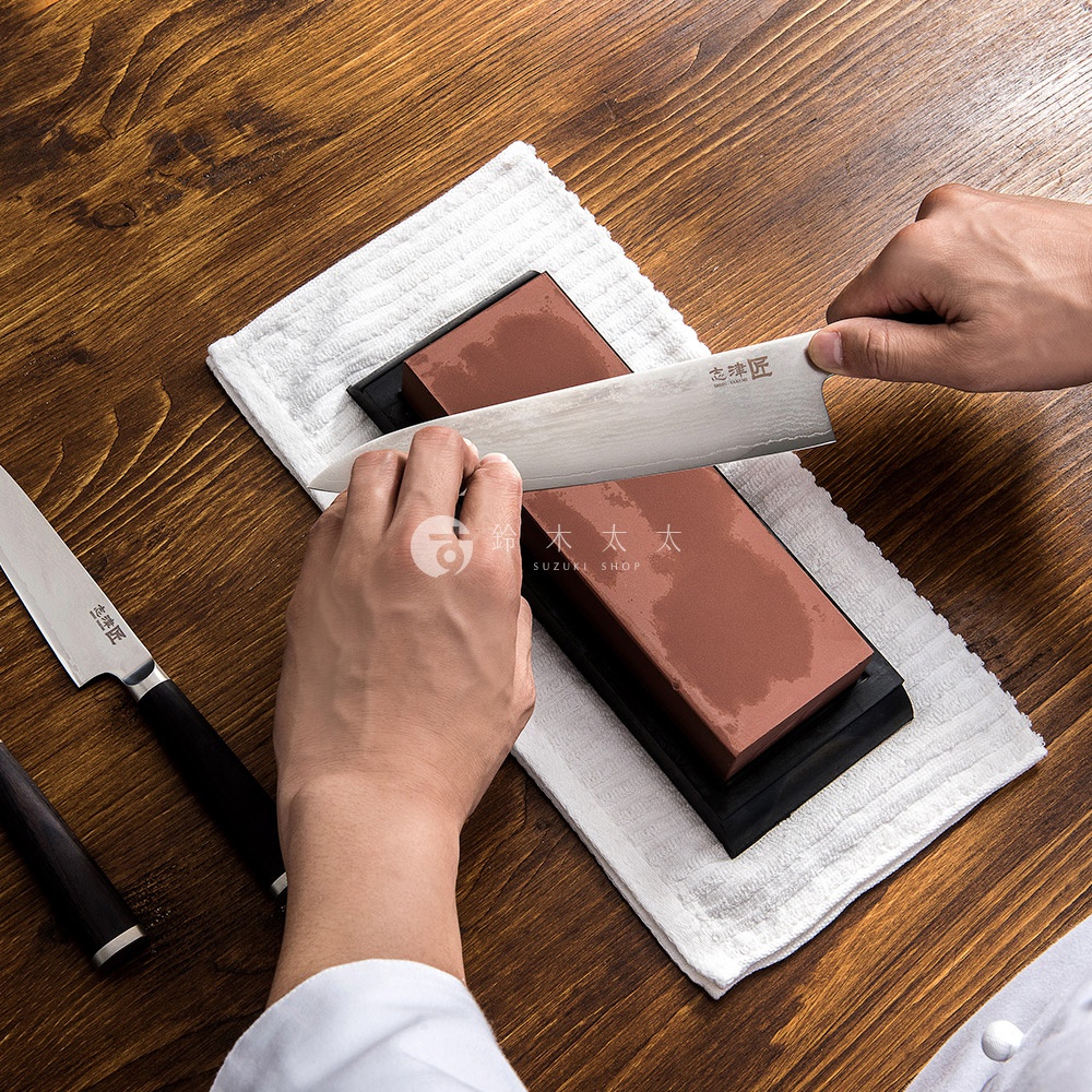 手中的志津匠磨刀石，沾濕後，正仔細地打磨著一把日式風格的廚刀。