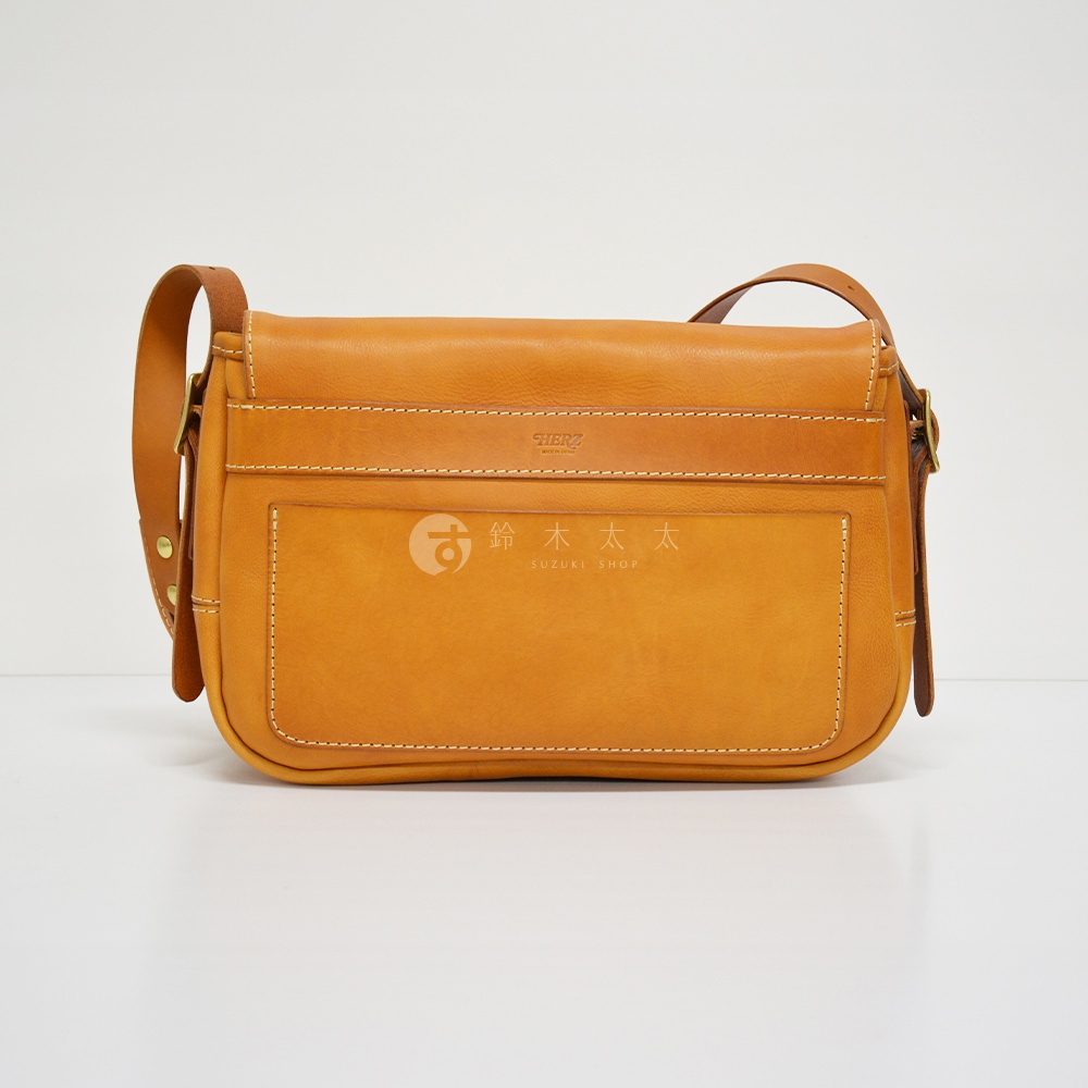 職人手作皮革復古翻蓋郵差包，呈現溫潤的焦糖棕色，採用厚實皮革製作，車縫線清晰。包款設有翻蓋式主袋及前方置物袋，搭配可調整長度的皮革背帶，散發經典復古風格。