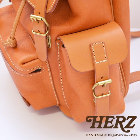 職人手作的復古棕色皮革旅行後背包，擁有雙層前袋設計，袋蓋以皮帶和金屬扣固定，搭配精緻的縫線細節。