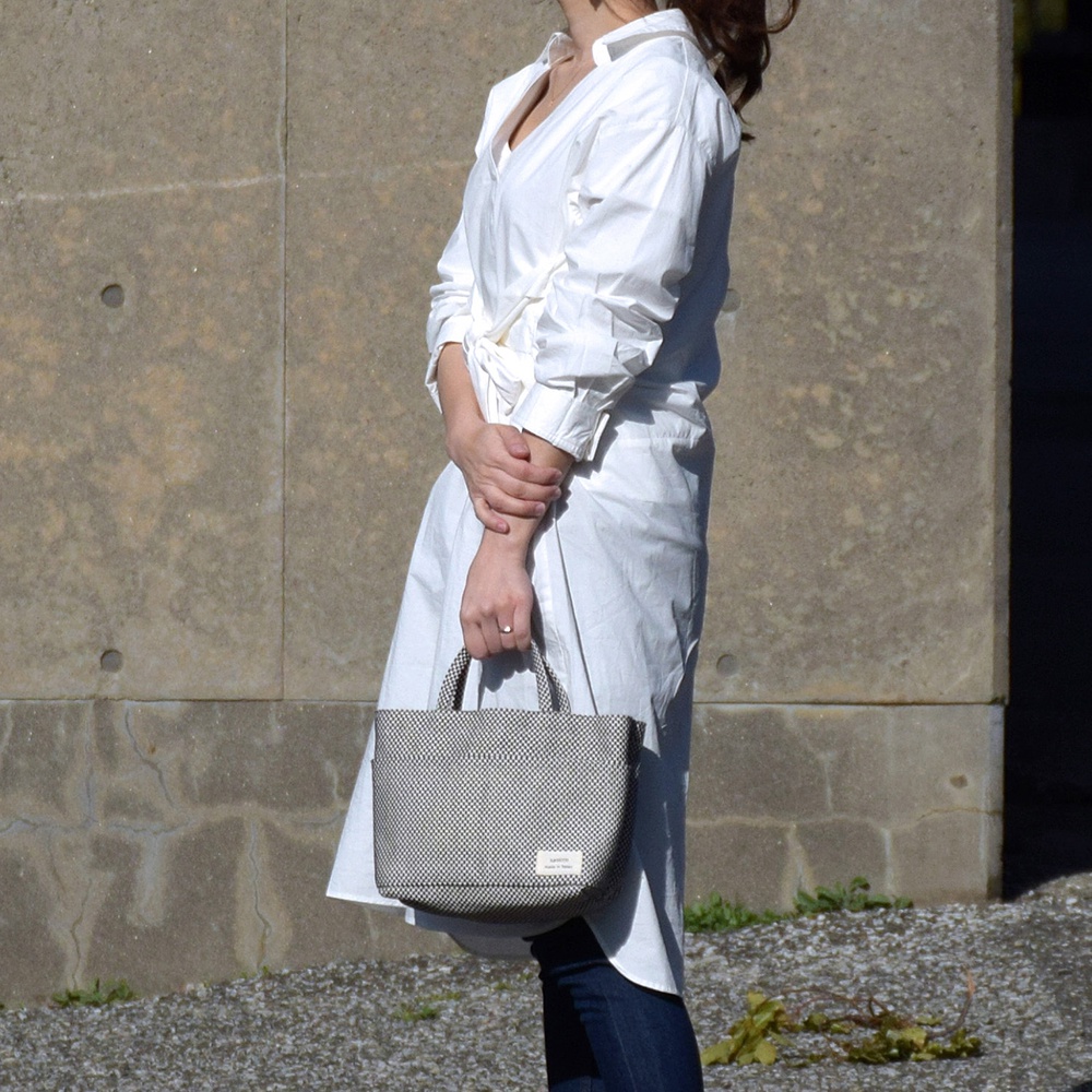 身穿白襯衫的女性手提著一個黑色與白色格子圖案的刺子織多口袋托特包，包上有品牌標誌。