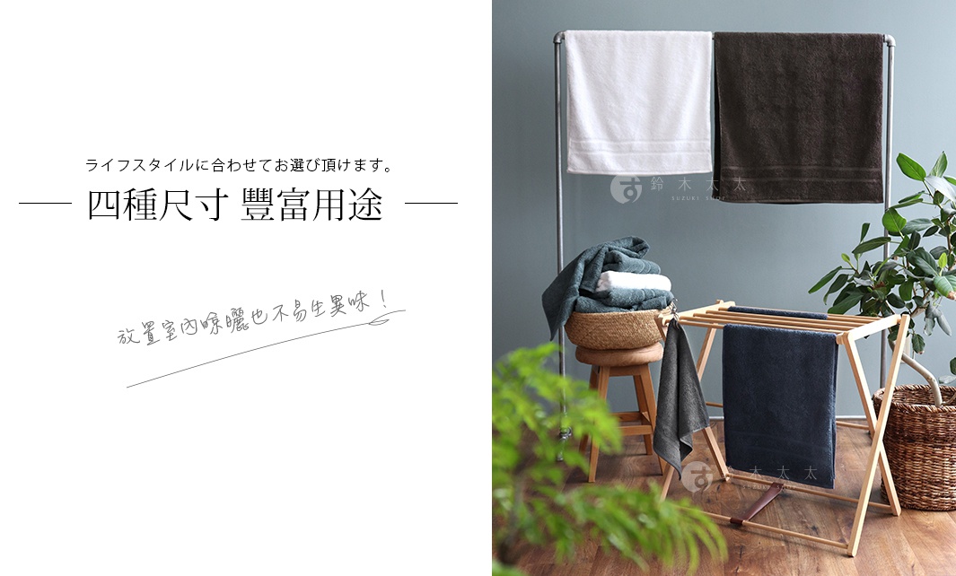 展示了兩條毛巾，一條白色，一條深棕色，懸掛在金屬架上。下方有一個木製曬衣架，上面有深藍色和深灰色的毛巾，旁邊還有一個草編籃和一盆綠葉植物。