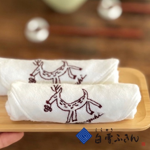 白色棉質方巾，繡有深紅色鹿的圖案，鹿口含著小花。兩條方巾疊放在淺色木盤上。