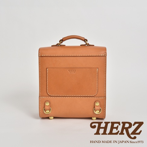 職人手作皮革經典學院風迷你後背包，採用天然棕色皮革，簡約方形設計，正面附有方形口袋和品牌標誌，頂部有提把，底部有金屬扣環，展現復古質感。