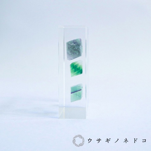 透明樹脂塊內嵌三塊不同深淺綠色螢石切片標本，呈現八面體晶體結構。