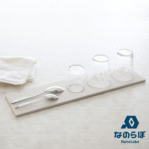 長形灰白色珪藻土置物墊，表面有細長條紋，上面放有兩把銀色湯匙和三個透明玻璃杯，左側疊放著一條白色毛巾。