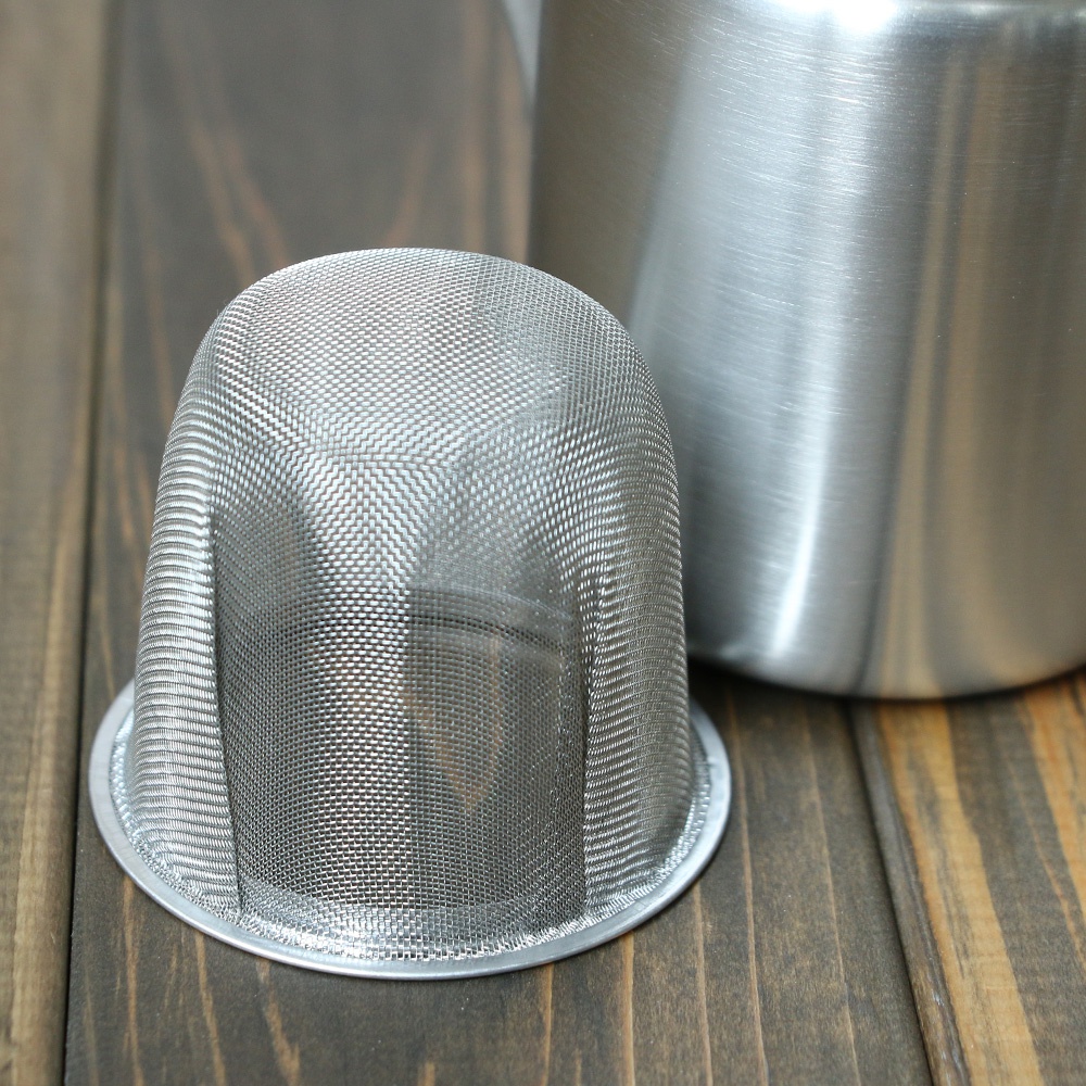 霧面不鏽鋼直筒茶壺，配有細濾網茶漏，側邊有把手，整體為銀色金屬材質，放置於木紋桌面上。