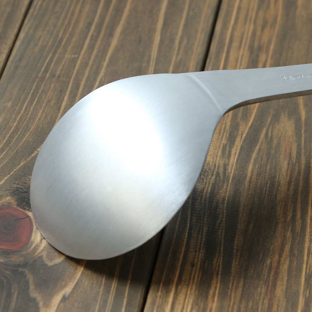 銀色鋁製湯勺，具有錘目紋飾，勺柄末端有細微刻字，置於深色木紋背景上。