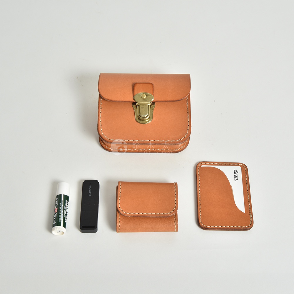 一個棕褐色真皮腰包，上方有一個黃銅鎖扣，旁邊擺放著一個潤唇膏、一個黑色電子設備和一個卡夾。