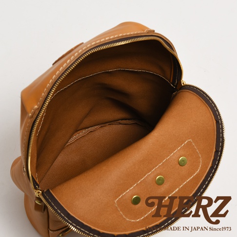 職人手作皮革大開口圓角後背包，展示棕褐色皮革材質，內部空間寬敞，附有拉鍊開合及金屬卯釘裝飾。