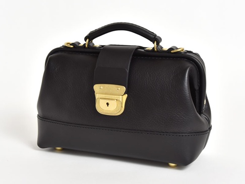 黑色皮革迷你口金包，附有金色鎖扣和提把，底部有四個金色腳釘。