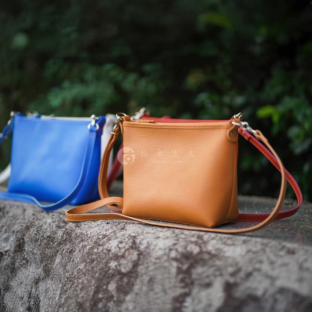 兩款京都職人手作隨身側背包，一款為亮藍色，另一款為淺棕色，皆為方形設計，配有可拆卸的同色系或對比色皮革背帶，採用粒面皮革材質，質感細緻。