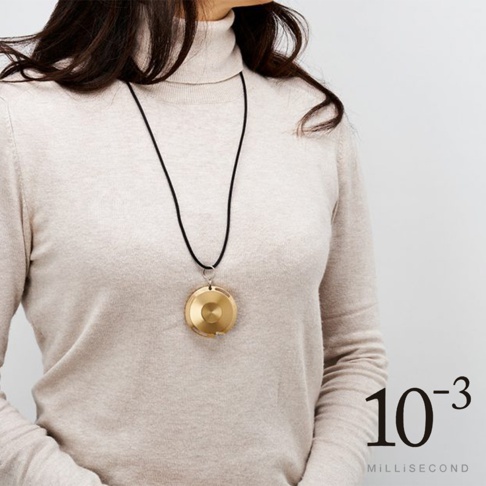 金色鋁製圓形卷尺，直徑約 5 公分，懸掛於黑色繩索上，由身穿米色高領毛衣的女性佩戴。