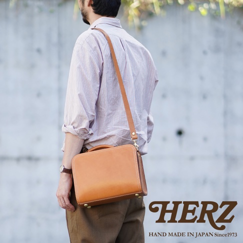 職人手作皮革兩用方形單肩包，採用棕色皮革，配有可調式長背帶及提把，包身有縫線細節與金屬卯釘。