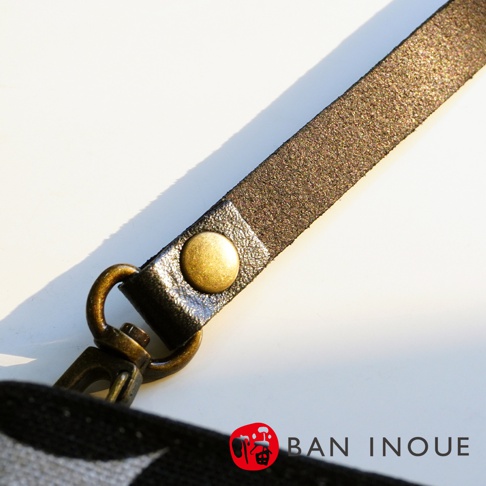 BAN INOUE 標誌旁的品牌名稱，以黃銅色金屬扣件固定在黑色皮革帶上
