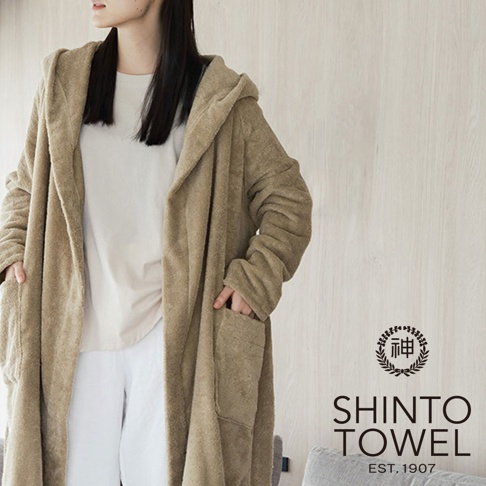 一名女子身穿淺棕色連帽蓬鬆浴袍，浴袍為長袖設計，兩側有口袋，材質看起來柔軟舒適。