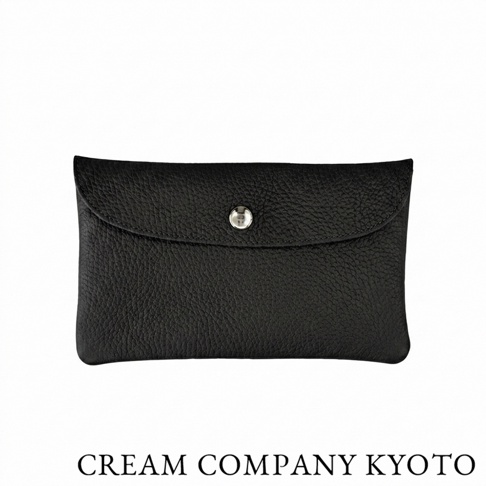 這款來自 CREAM COMPANY KYOTO 的黑色皮革手拿包，表面呈現自然的細緻荔枝紋路，包蓋中央配置一枚簡潔的金屬按釦，整體設計展現日本職人手作的極簡質感，適合作為收納卡片或隨身小物的多功能配件。