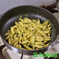 一個裝滿青醬筆管麵的平底鍋，鍋身為深灰色，鍋柄為木質。