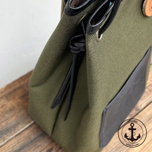 從特寫鏡頭看，一個綠色的防潑水尼龍束口包，搭配義大利皮革裝飾，上面有一個名為 clueto 的錨形標誌。