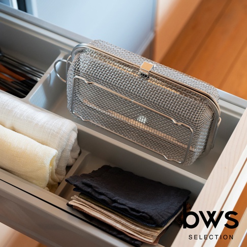 不鏽鋼網狀清潔收納盒，帶有銀色金屬提把和扣環，放置於抽屜中，旁邊有捲起的白色和米黃色布料，以及疊放的多色小方巾。