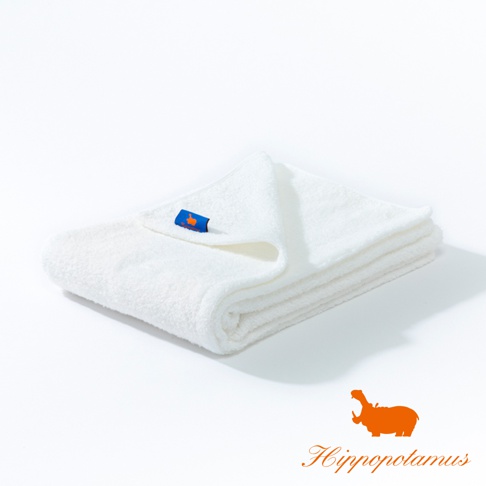 展開的白色竹棉混紡厚感大浴巾，一角縫有藍色標籤，上印橘色河馬圖案。