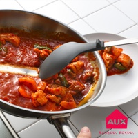 一隻深灰色矽膠不沾桌拌炒量匙，正從不鏽鋼鍋中舀起燉煮的雞肉與紅椒塊，湯汁呈橘紅色。