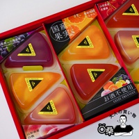 一盒裝有八個三角形果凍，顏色包含紫色、橘色、紅色及粉紅色。果凍外層為透明塑膠包裝，上面印有金色貼紙，標示品牌名稱「DELUXE」及「GELÉE TRIANGLE」。包裝盒內有不同口味的水果插圖，如葡萄、柑橘和櫻桃。