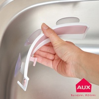 粉色與白色組合的廚餘架，具有可開合設計，以吸盤固定於水槽邊緣，架上有一粉色掛勾。