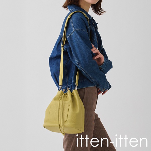 itten-itten 品牌 logo 旁，一位女性身穿丹寧外套，肩背一個芥末黃色的荔枝皮革束口水桶包。
