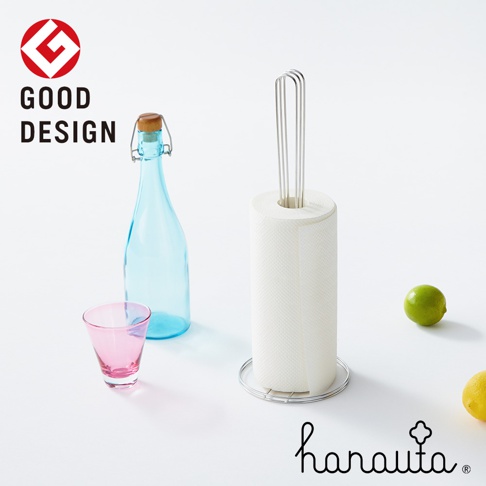 不鏽鋼立式紙巾架，帶有圓形底座和頂部金屬支架，可容納捲狀紙巾。旁邊有一個藍色玻璃瓶、一個粉紅色玻璃杯、一顆青檸和半顆檸檬。