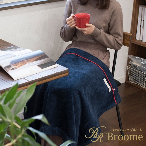 深藍色羊毛觸感膝蓋毯，邊緣飾有細紅色滾邊，蓋在一位坐在椅子上、手持紅色馬克杯的女士身上。