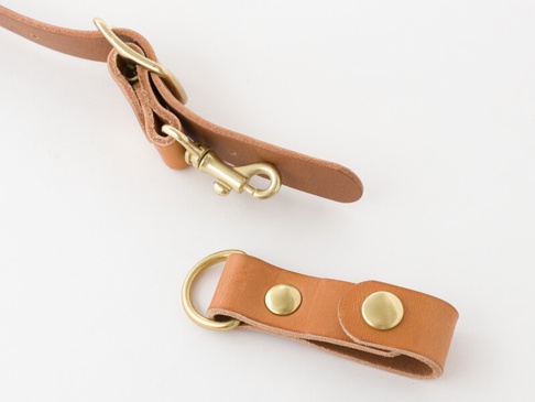 職人手作皮革背包用減壓胸前扣帶 (KO-2) 由淺棕色皮革製成，配有黃銅色金屬扣環、鉤扣和鉚釘，用於固定和調整。