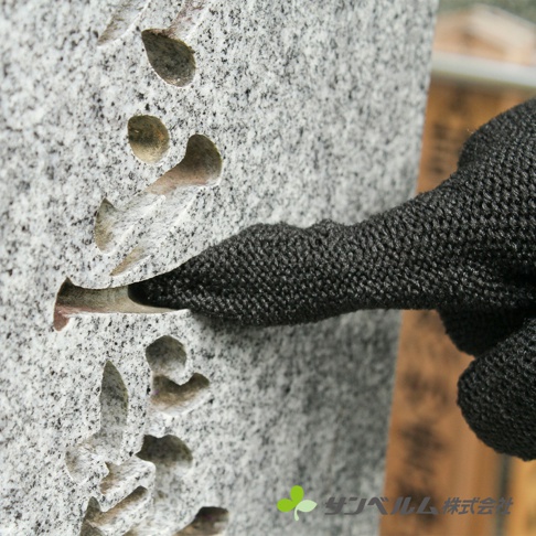 一隻黑色編織紋理的清潔手套，正伸入一個有淺灰色顆粒紋理的灰色石碑的凹槽中，石碑上刻有漢字。