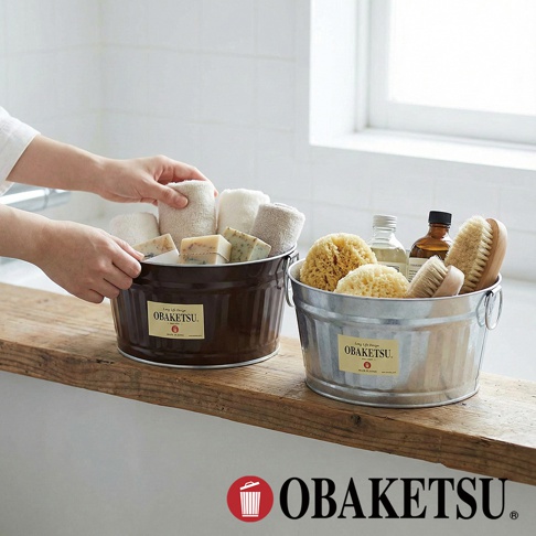 手工製 OBAKETSU 鍍鋅鋼迷你收納桶，裝有毛巾、肥皂、海綿和刷子，擺放在木質檯面上。