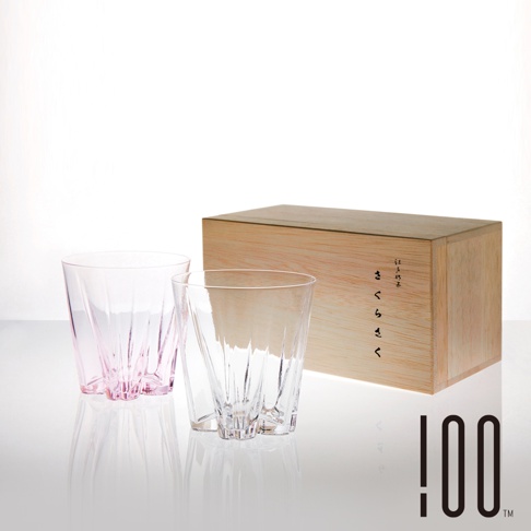 兩只玻璃威士忌杯，一只為粉紅色，另一只為透明色，皆帶有垂直刻紋設計，置於一個淺木色禮盒旁。
