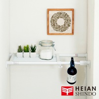 白色伸縮桿層架，架上擺放三個白色花盆內栽種的仿真植物、一個玻璃罐裝白色粉末，以及一個黑色噴霧瓶。層架下方懸掛著黑色噴霧瓶，上方牆面掛有一幅木框裝飾畫。