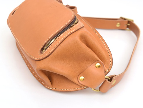 職人手作皮革拉鍊旅行斜背包 (F-7) 是一款棕褐色全皮革製成的斜背包，配有黃銅色拉鍊、縫線細節和可調節式皮革背帶，適合旅行使用。