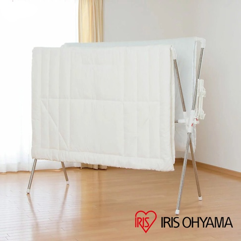 不鏽鋼X型曬衣架，附有白色塑膠零件，架上掛著一張白色菱格紋的棉被。