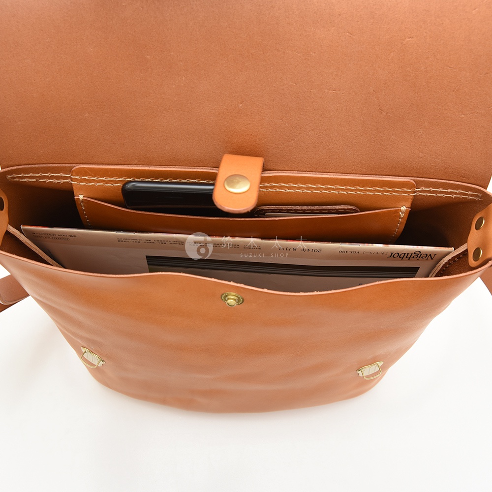 日本HERZ 職人手作皮革雙扣旅行郵差包，棕色牛皮革材質，內部可見手機、雜誌等物品，包口處有銅扣設計。