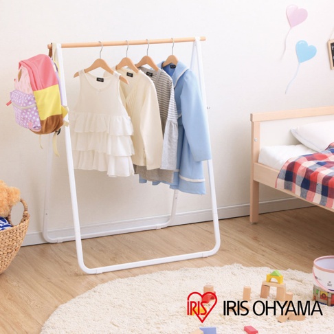 白色金屬框架搭配原木橫桿，掛有粉色、黃色、紫色拼色背包，以及白色荷葉邊洋裝、米白色毛衣、灰色條紋上衣和淺藍色長袖外套。