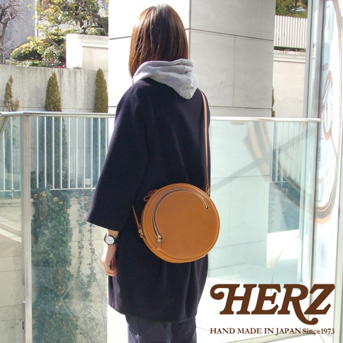 職人手作皮革小圓包，淺棕色，圓形包身，配有拉鍊開合和可調式側背帶。