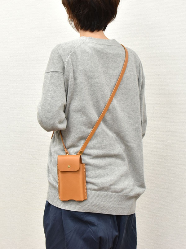 棕色皮革製成的手機收納包，款式簡潔，附有品牌標誌。包包配有一條可調節的細長肩帶，可斜挎或單肩佩戴。包身有縫線細節，整體呈現自然質樸的質感。